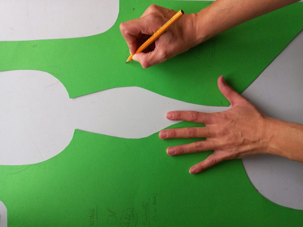 Mani che tracciano a matita un cartamodello su carta verde