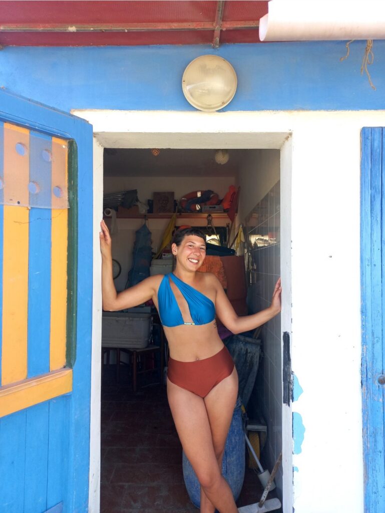 Ragazza sorridente in top Cabriolet azzurro e slip ruggine sulla porta di una cabina colorata
