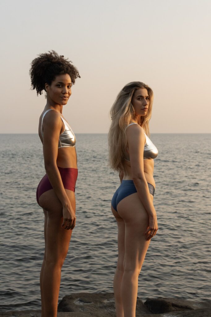 Due ragazze di schiena in bikini metallizzati, davanti al mare al tramonto