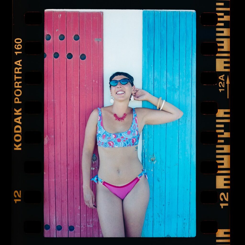Foto su pellicola: ragazza in top a fantasia e slip fucsia davanti a una porta rossa e azzurra