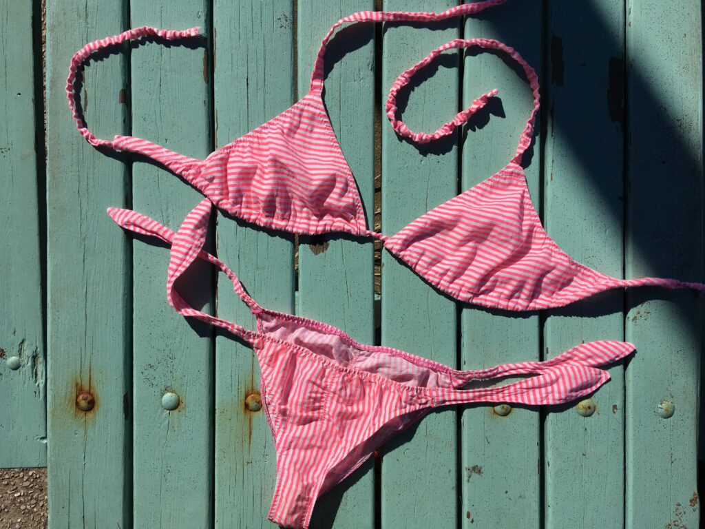 Bikini a triangolo rosa a righine steso su una porta verde