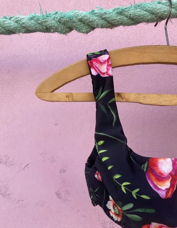 Top a fiori su fondo nero appeso a una gruccia, contro un muro rosa