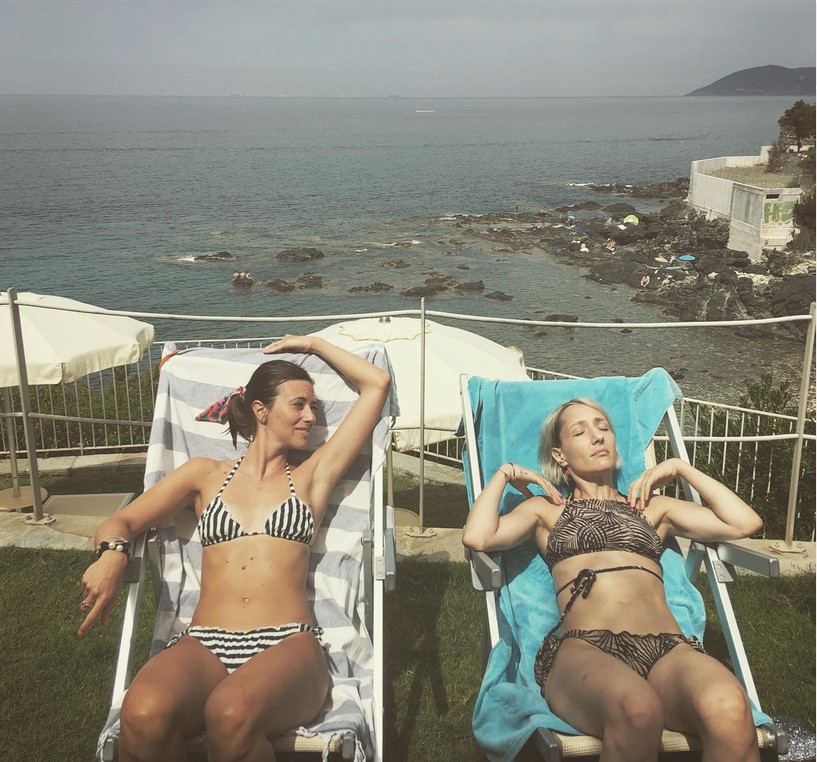 Due ragazze in bikini sulle sdraio, con il mare dietro