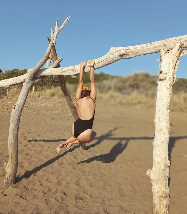 Girl in a black swimsuit hanging from a log on the beach